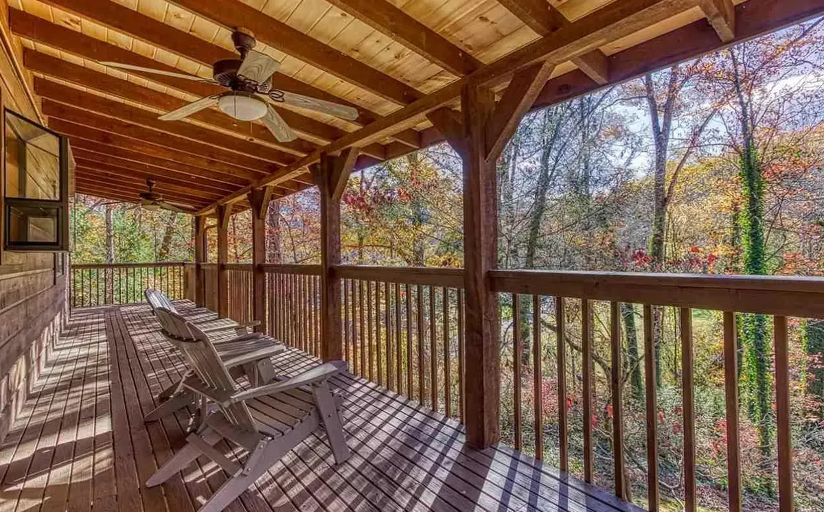 A spacious wooden deck surrounded by lush greenery and vibrant fall foliage. Adirondack chairs are arranged for conversation and relaxation, creating an inviting space for groups to gather and enjoy the outdoors.