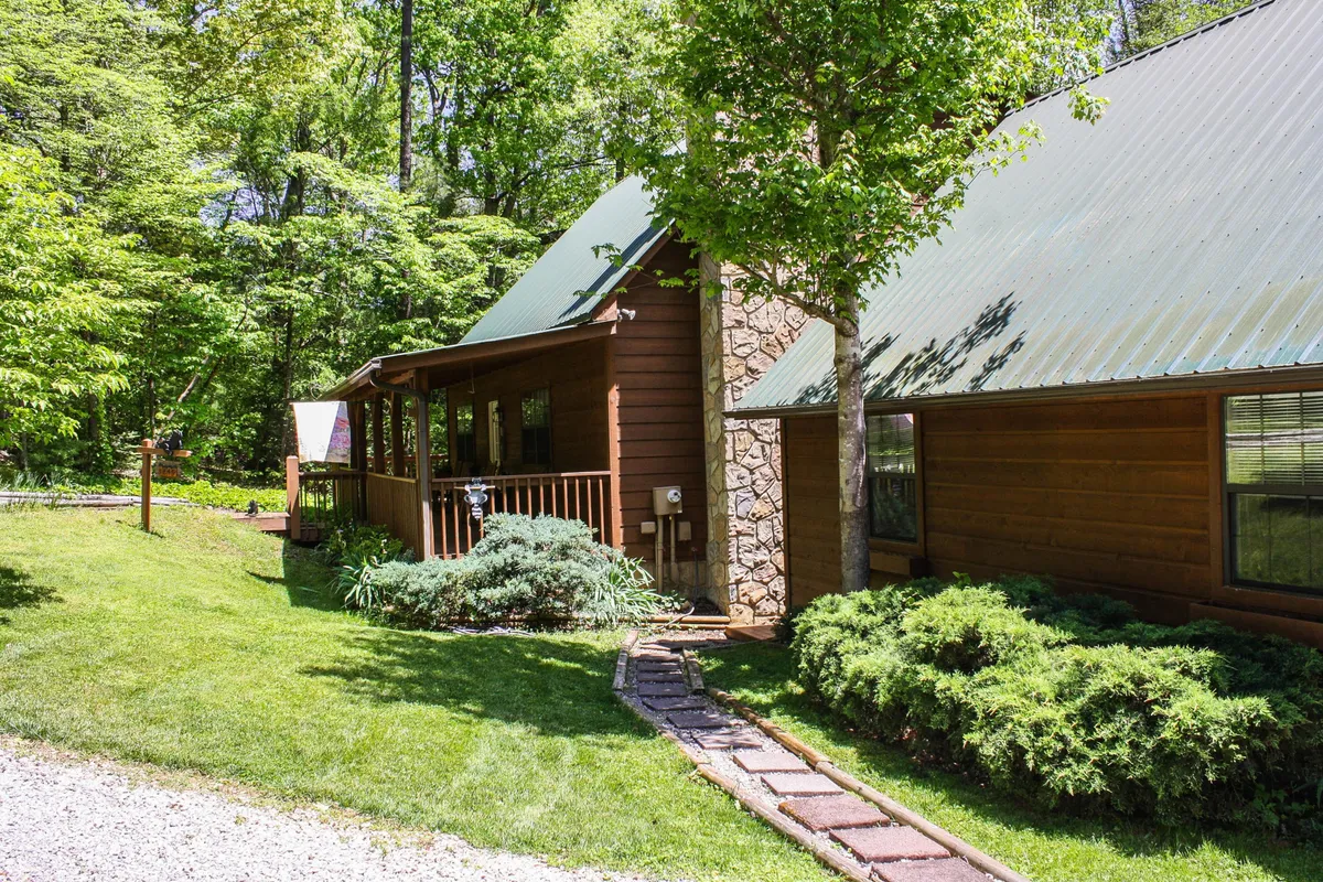 A rustic wooden structure accented by stone and surrounded by lush green foliage, with a pathway leading up to a tranquil porch. The setting is ideal for morning coffee or evening gatherings, emphasizing the cabin’s proximity to nature and opportunities for outdoor family moments.