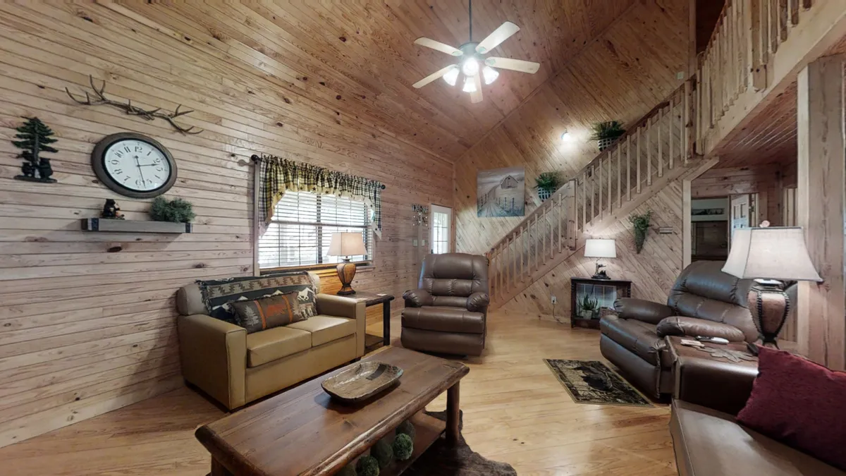 A warm and welcoming interior space with reclining chairs, a wooden table ideal for group activities, and a prominent wall clock. The setting is cozy, suggesting a space suited for storytelling by the fireplace or group celebrations.