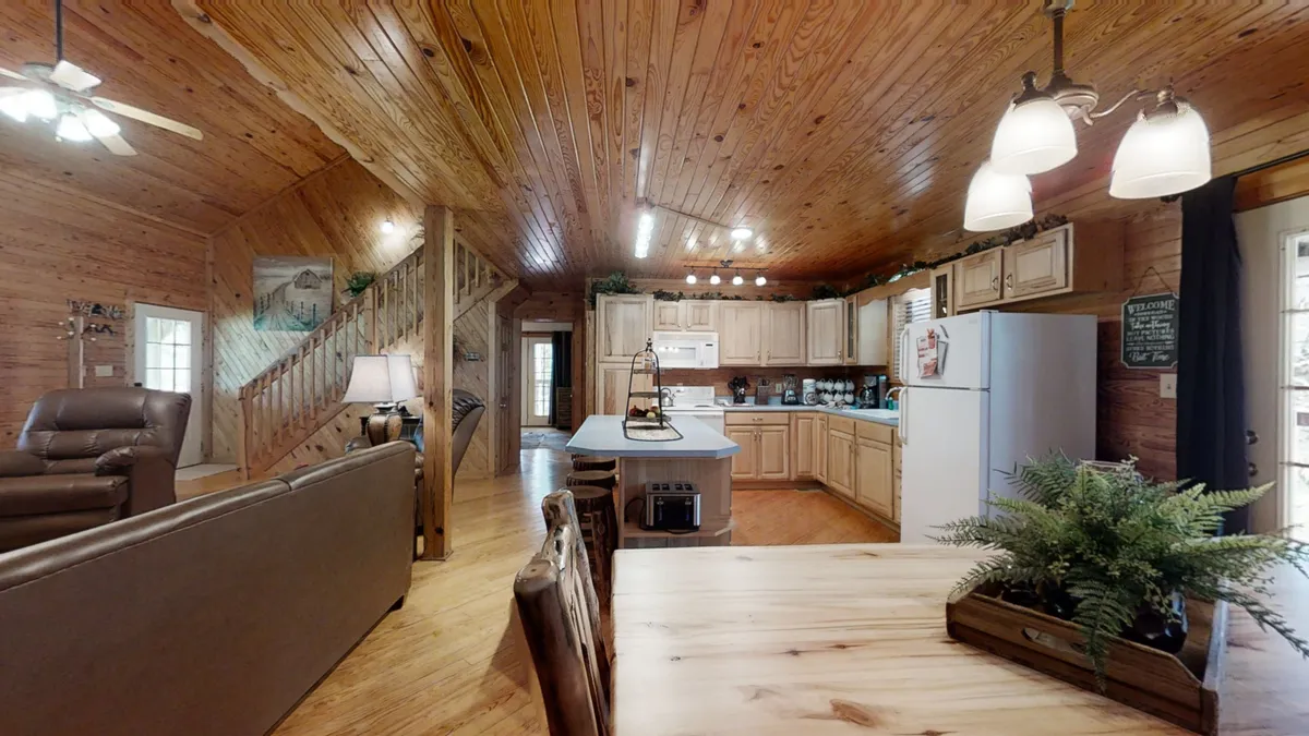 An open-concept space featuring exposed wooden beams, a kitchen island, and a dining table. The area is styled for both cooking and gathering, with sightlines connecting the kitchen and dining areas—a versatile layout ideal for socializing.