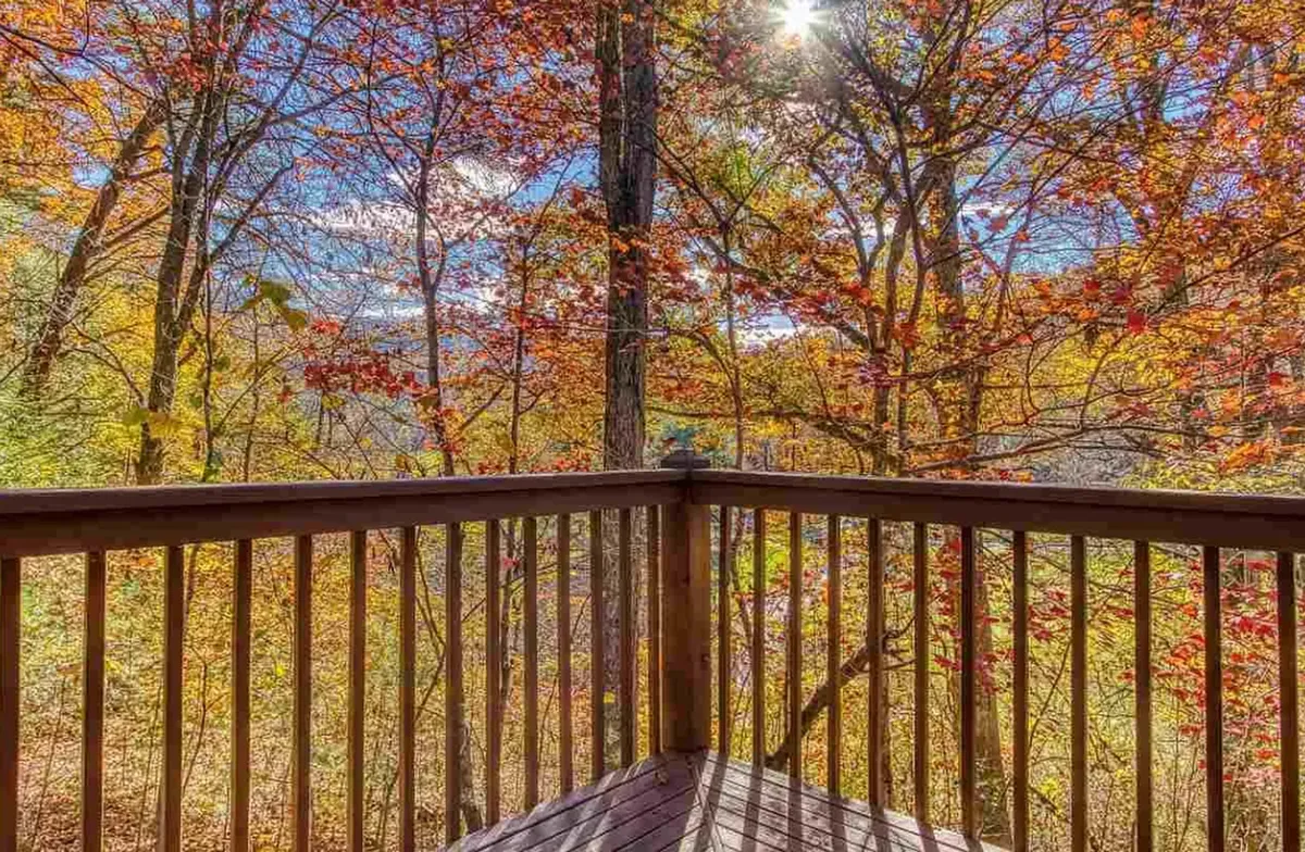 A peaceful deck with wooden railing overlooks colorful foliage and rolling hills, suggesting a seamless blend of comfort and nature. The outdoor space is ideal for relaxing, bird watching, or stargazing after a day of adventure.